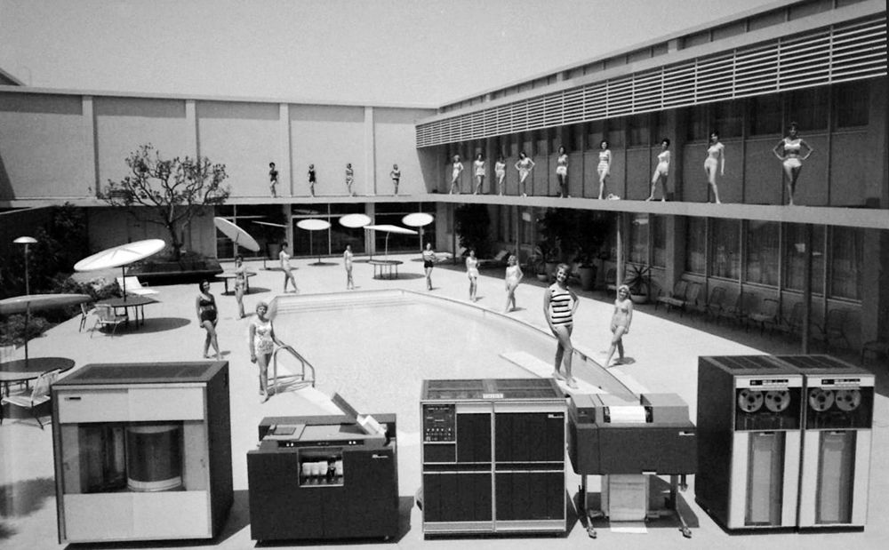 Archival black-and-white poolside scene with large computers arranged in the foreground.